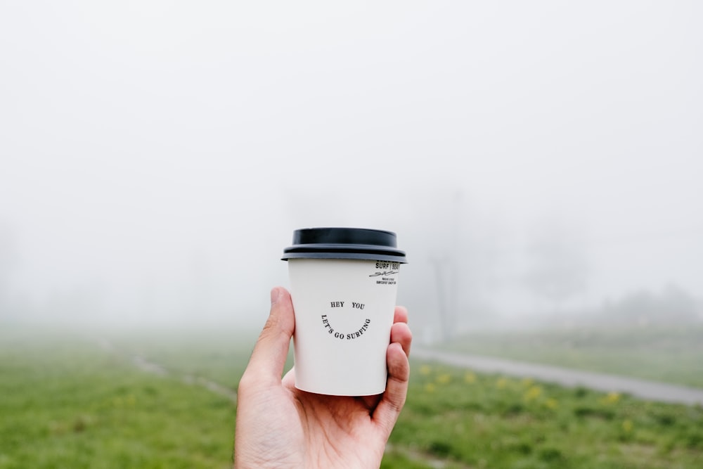 a hand holding a cup of coffee in a foggy field