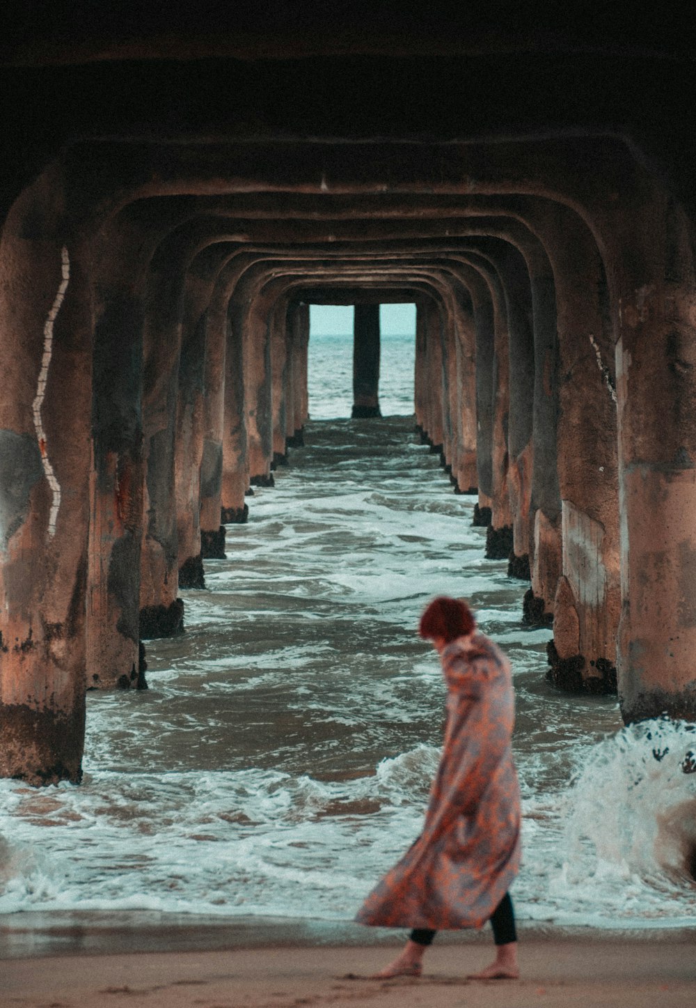 a woman walking on a beach under a pier