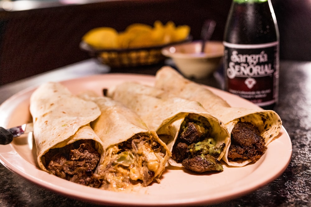 a burrito cut in half on a plate next to a bottle of beer