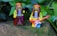 Two LEGO figurines dressed in hippie-style clothing are placed outdoors against a backdrop of green leaves. One figure is holding a black camera, while the other holds a red electric guitar.