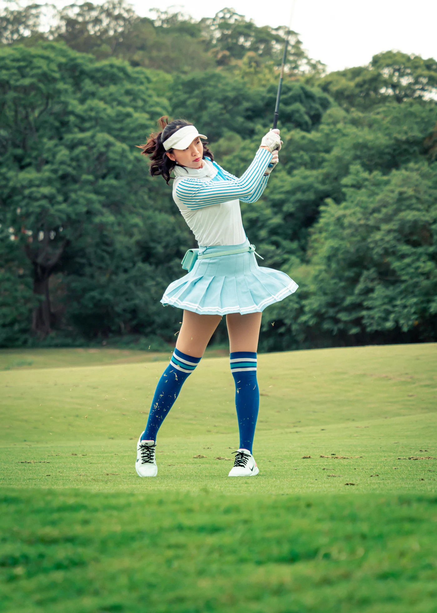 Female golfer in a pale blue outfit finishing her swing