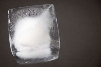 Close-up of a crystal-clear ice cube melting slowly on a sleek glass surface.
