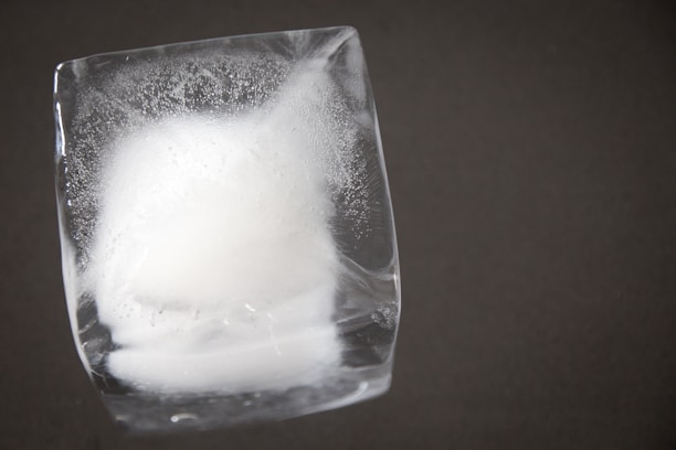 Close-up of a crystal-clear ice cube melting slowly on a sleek glass surface.