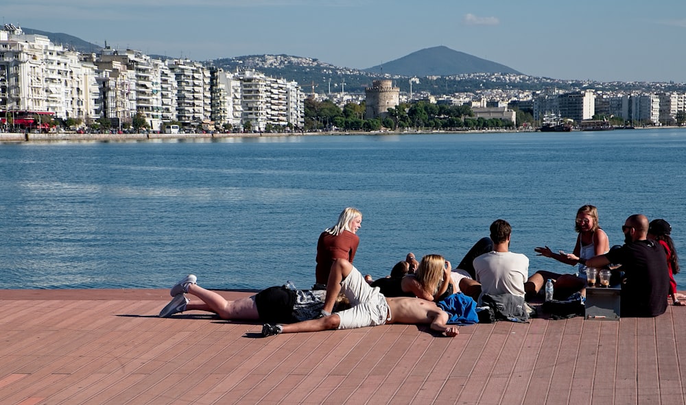 a group of people sitting on a pier next to a body of water