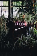 a neon sign that reads flow next to some plants