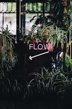 a neon sign that reads flow next to some plants