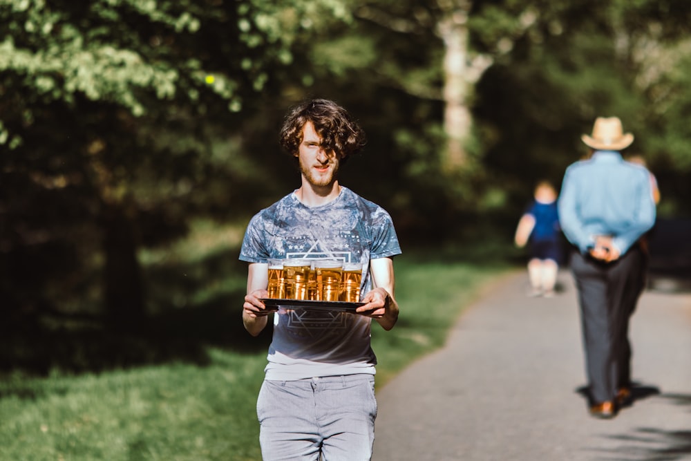 a man walking down a road carrying a tray of beer