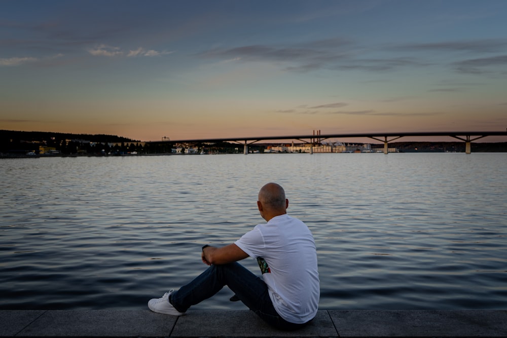 a man sitting on the edge of a body of water