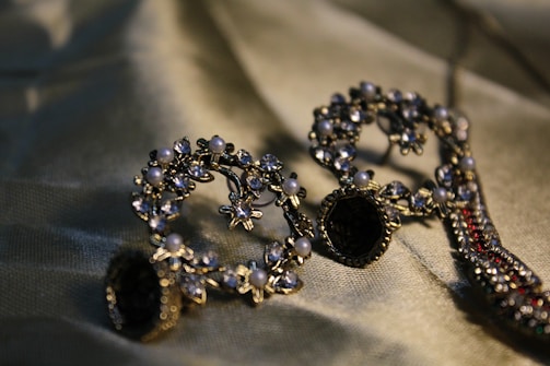 Intricately designed earrings adorned with small pearls and crystals are arranged artistically on a silky fabric backdrop, reflecting light and showcasing their elaborate craftsmanship.