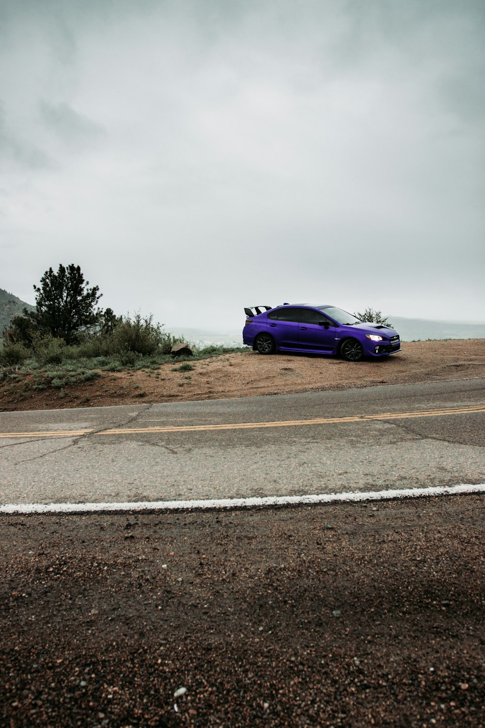 Cupé púrpura en una carretera de asfalto gris bajo un cielo nublado gris durante el día