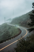 A winding mountain road with a taxi driving through misty Ooty hills.
