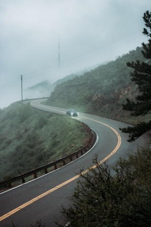 A winding mountain road with a taxi driving through misty Ooty hills.