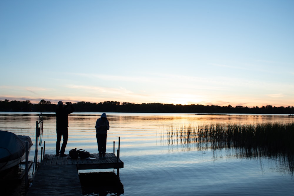a couple of people standing on a dock next to a body of water