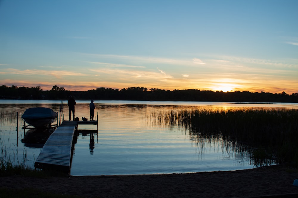 a couple of people standing on a dock next to a body of water