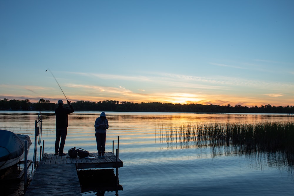 a couple of men standing on top of a pier next to a body of water