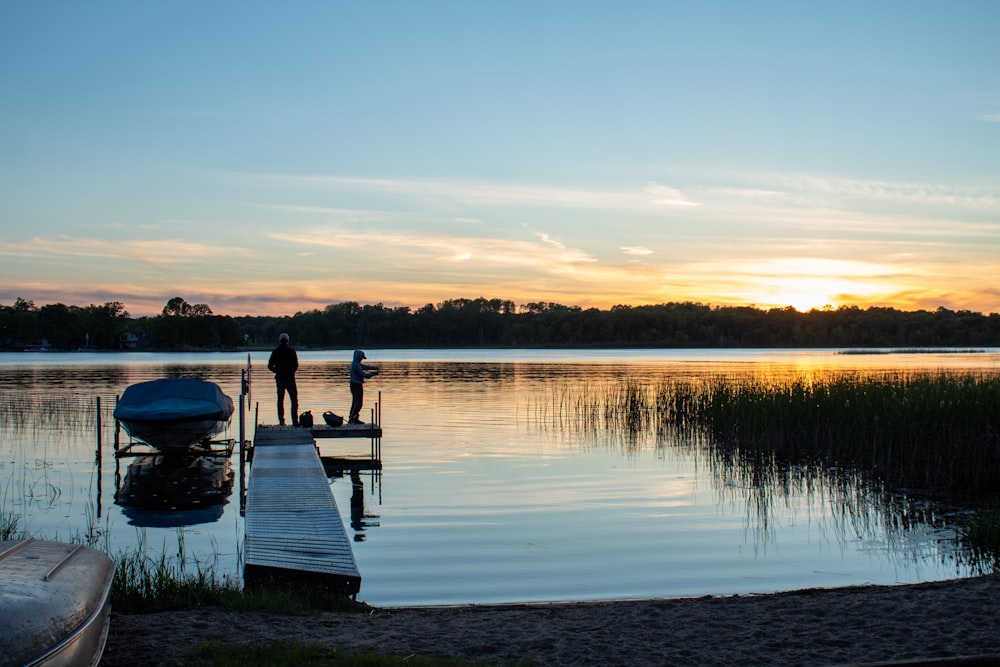 a couple of people standing on a dock next to a body of water