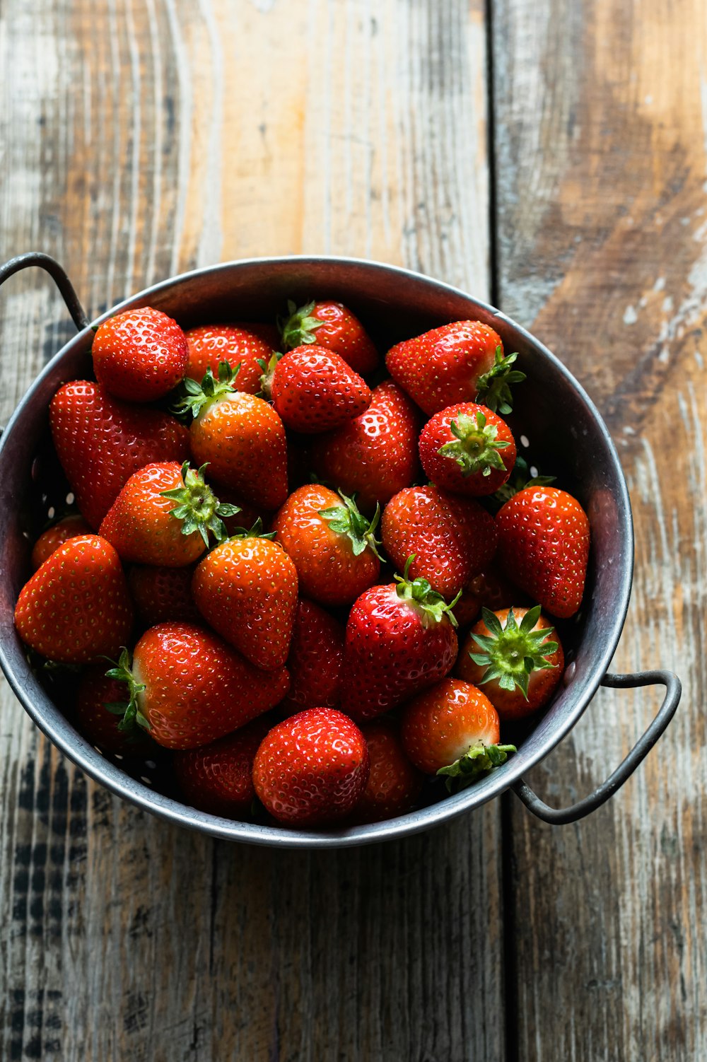 a metal bowl filled with lots of ripe strawberries