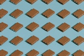 A repeating pattern of rectangular cookies or crackers with a creamy filling, arranged neatly on a blue background in a grid layout. The cookies are identical and evenly spaced, creating a sense of uniformity.