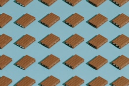 A repeating pattern of rectangular cookies or crackers with a creamy filling, arranged neatly on a blue background in a grid layout. The cookies are identical and evenly spaced, creating a sense of uniformity.
