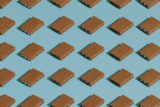 A repeating pattern of rectangular cookies or crackers with a creamy filling, arranged neatly on a blue background in a grid layout. The cookies are identical and evenly spaced, creating a sense of uniformity.