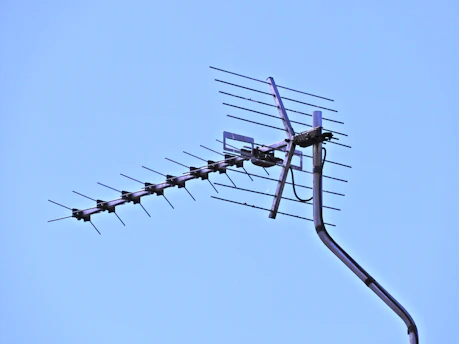 A close-up of a homemade antenna mounted on a backyard mast against a clear blue sky.