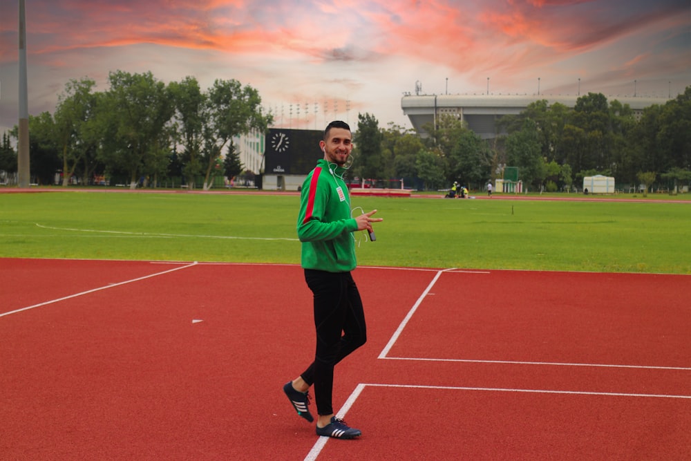 man in green long sleeve shirt and black pants standing on track field during daytime