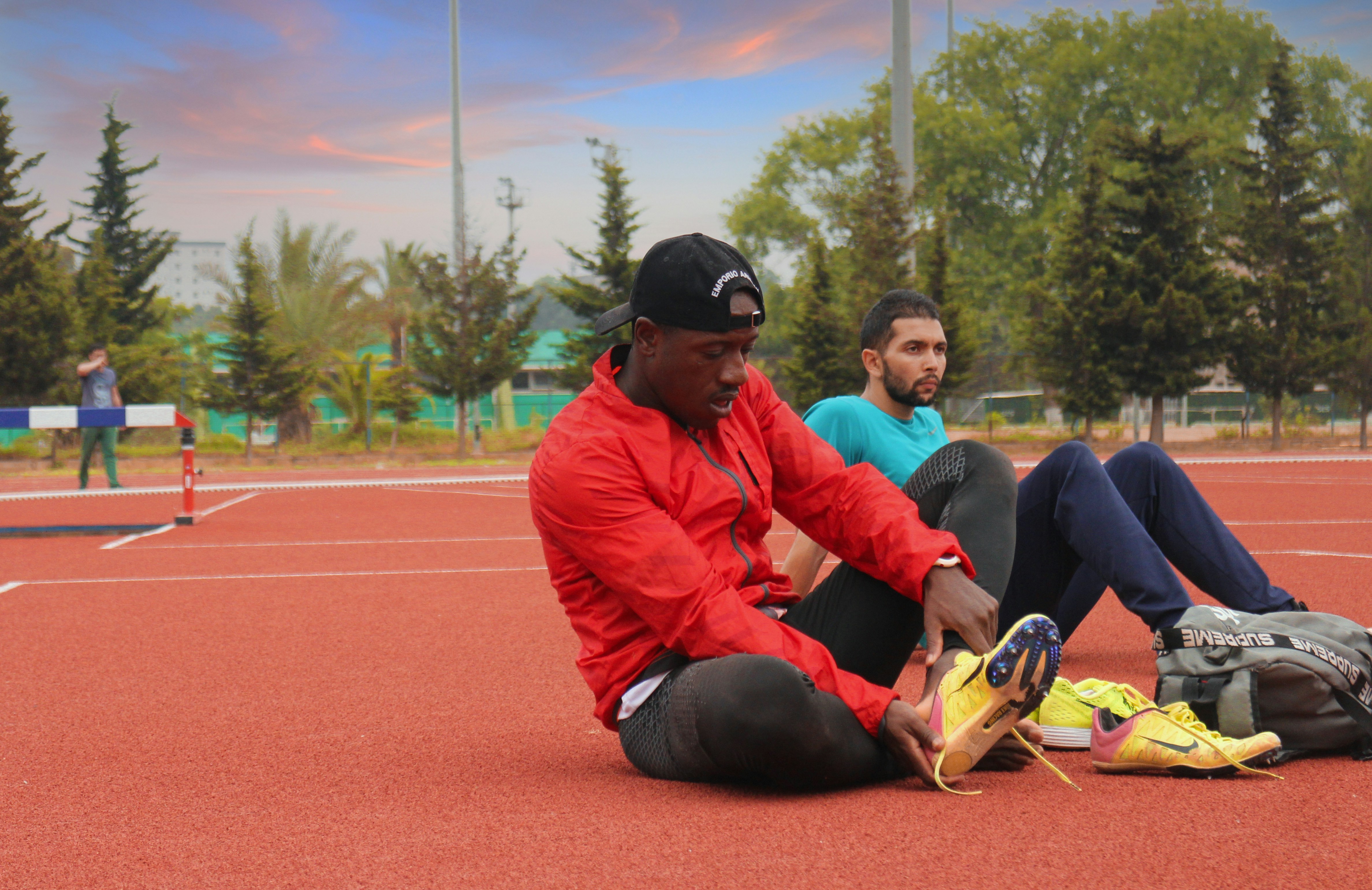 man in orange jacket and black pants sitting on ground during daytime