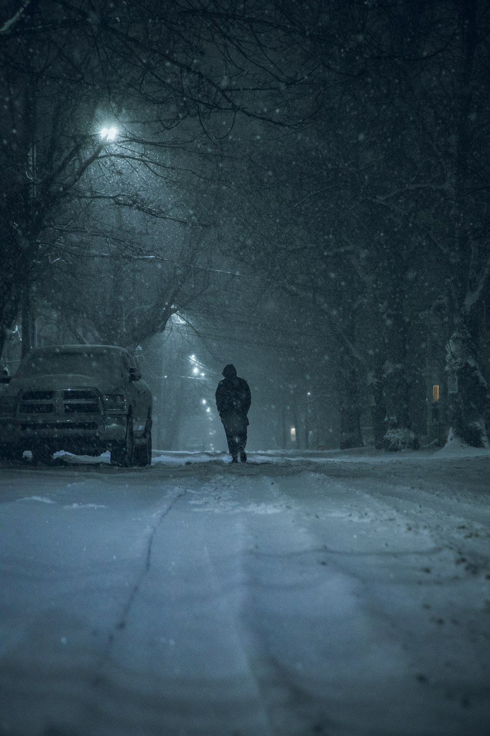 Person in schwarzer Jacke steht nachts auf schneebedeckter Straße