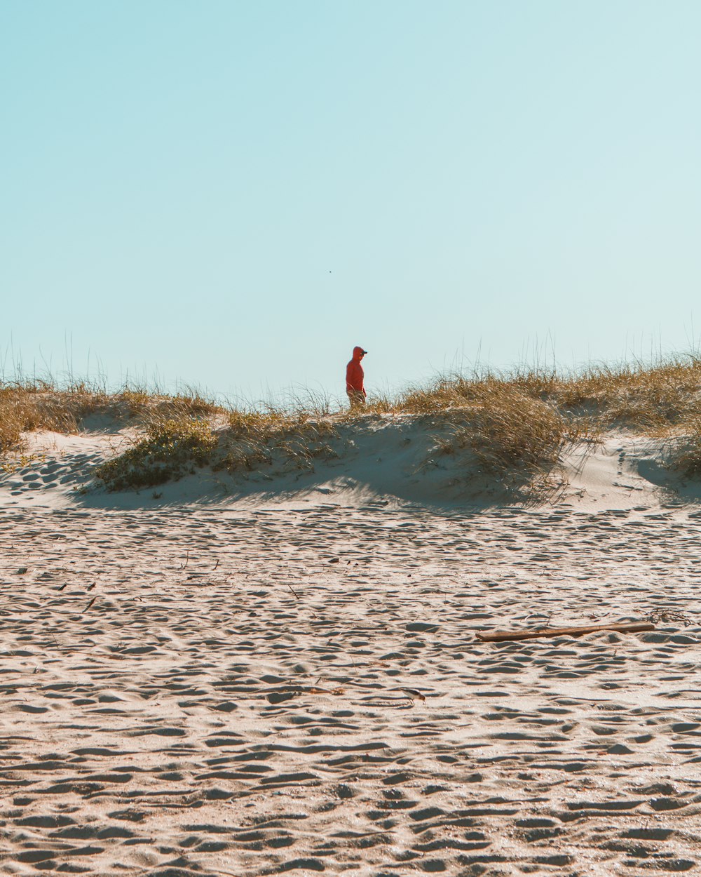 Person in rotem Hemd und schwarzer Hose, die tagsüber auf braunem Sand steht