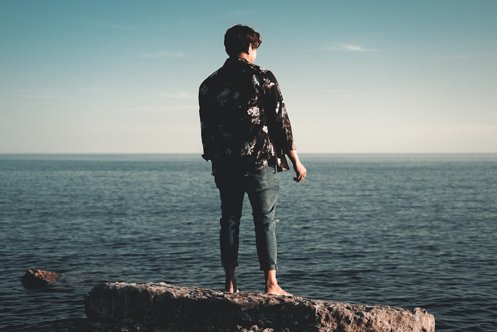 man in black jacket standing on rock near sea during daytime