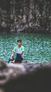 An individual sitting calmly on a rock, gazing thoughtfully at a flowing river.