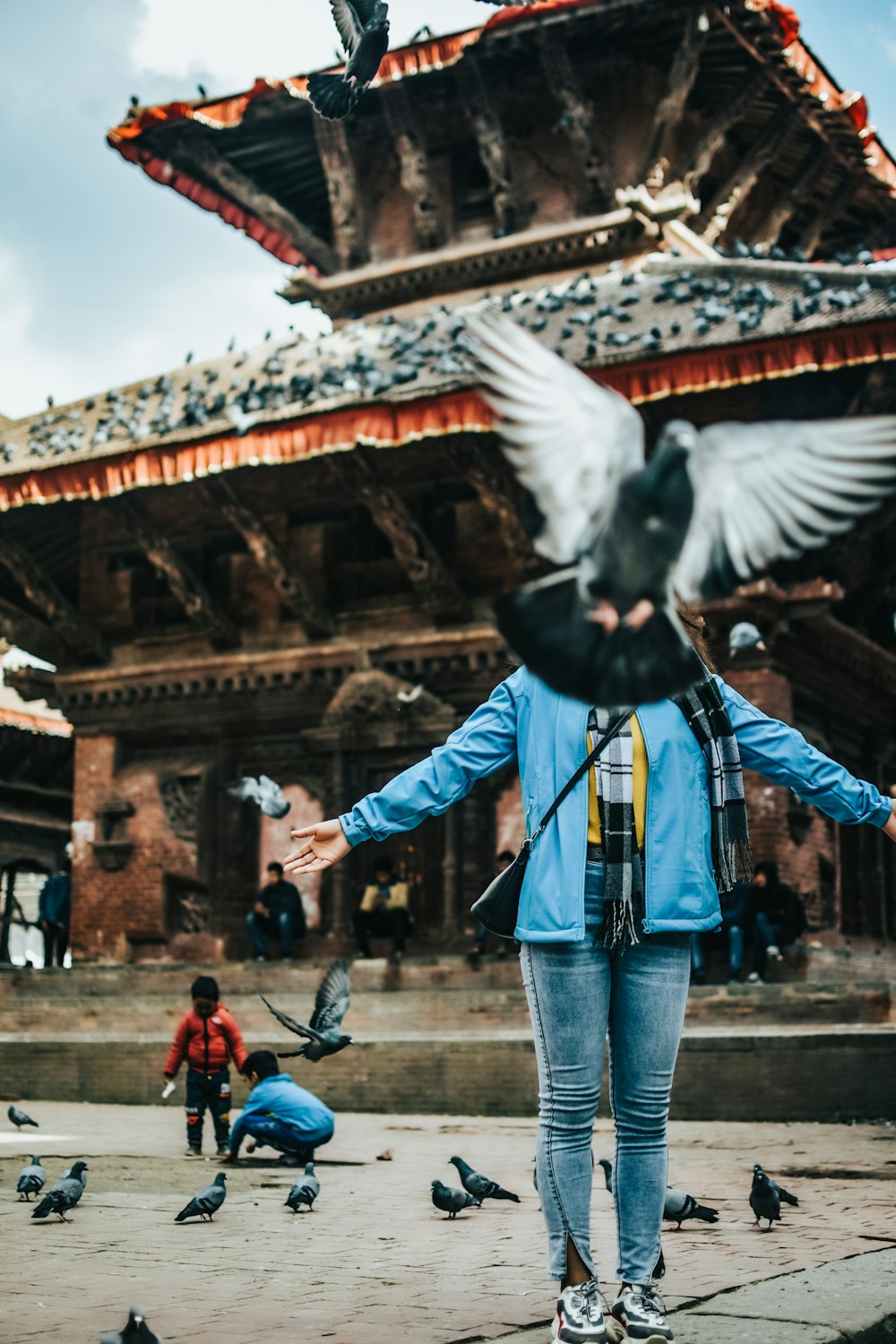 man in blue jacket and blue denim jeans standing in front of black and white bird