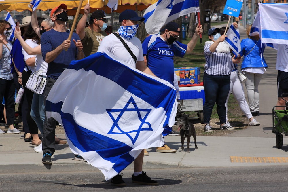 Des gens portant des drapeaux bleus et blancs marchant dans la rue pendant la journée