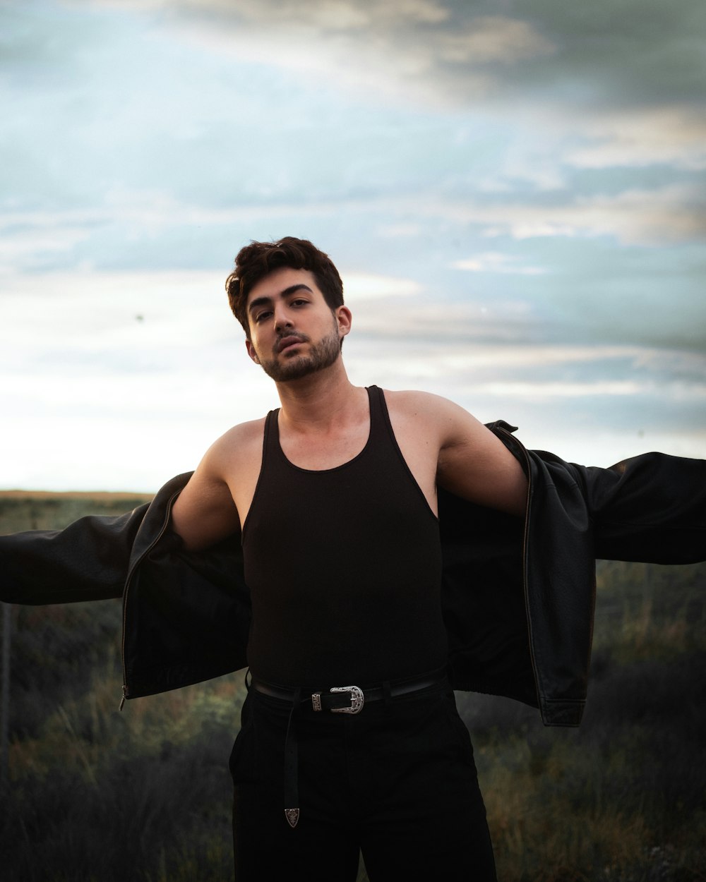 man in black tank top standing on green grass field under white clouds during daytime