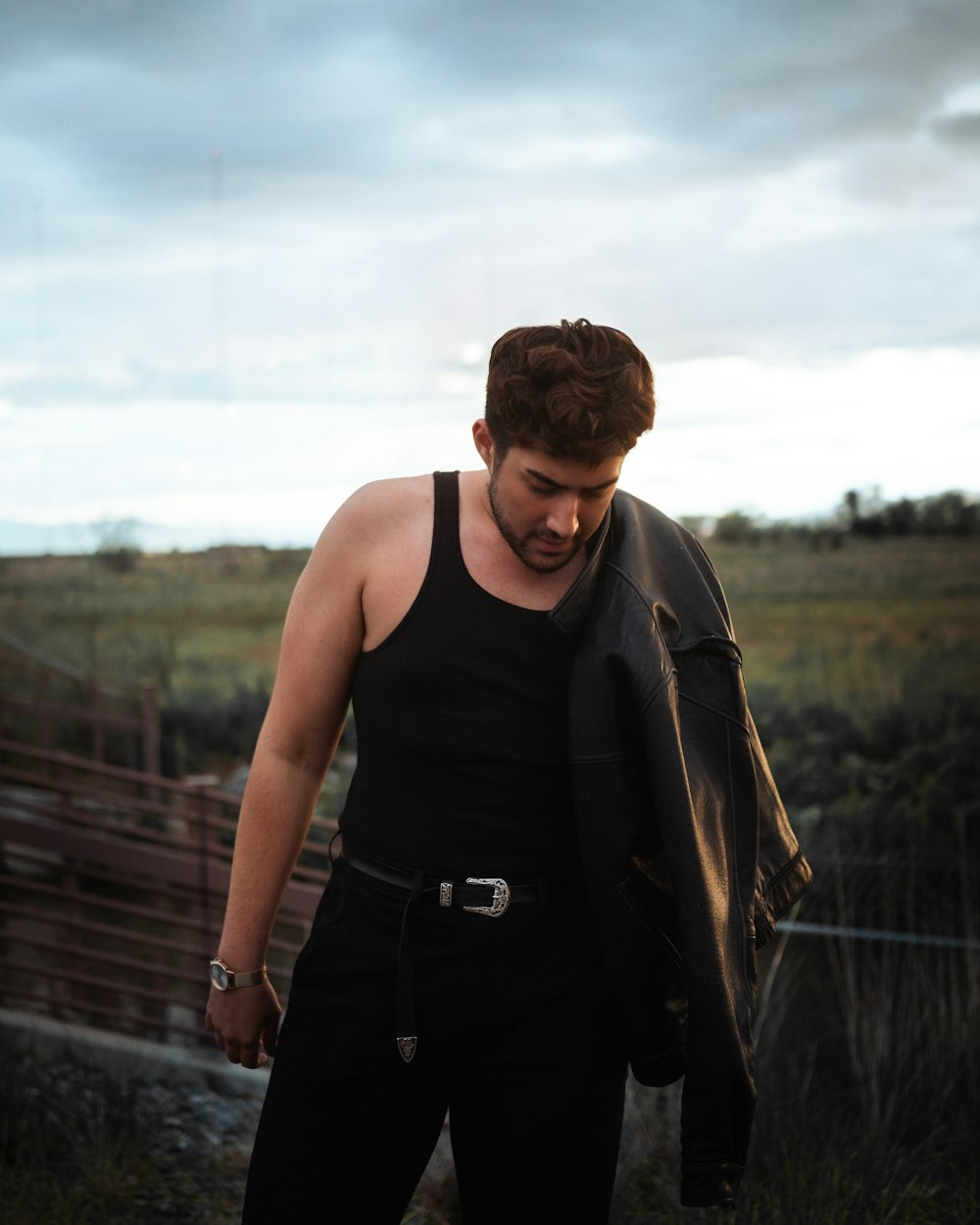 man in black tank top and brown jacket standing on wooden bridge during daytime