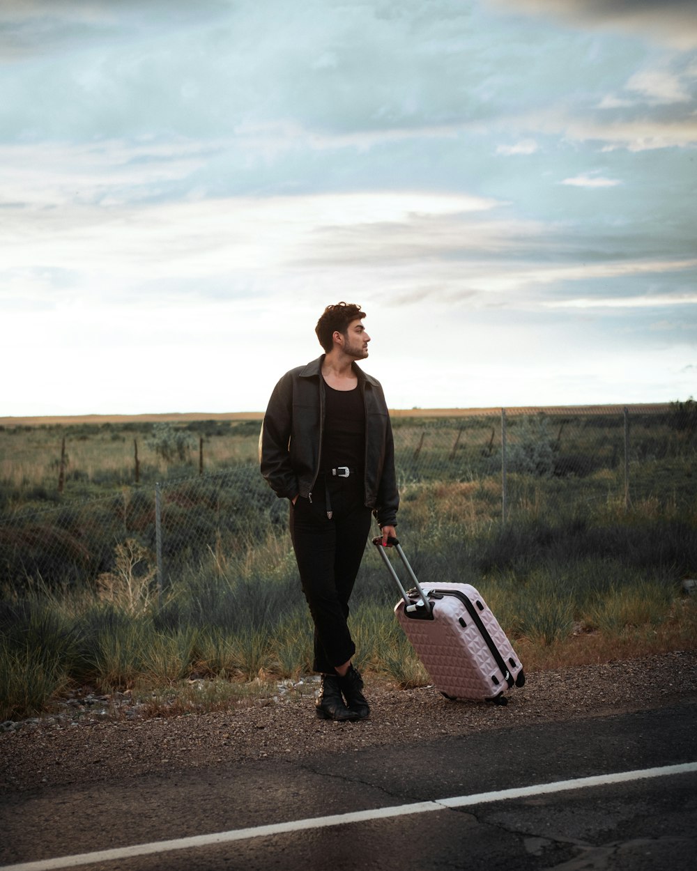 man in black jacket holding black and white shopping cart walking on dirt road during daytime