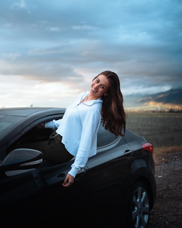 woman in white long sleeve shirt leaning on black car
