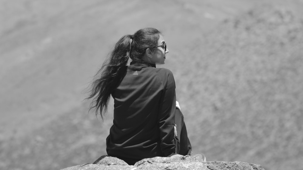 grayscale photo of woman in black long sleeve shirt sitting on rock