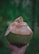 A fresh coconut is held up by a hand against a blurred green background. The top of the coconut is cut open, exposing the interior.