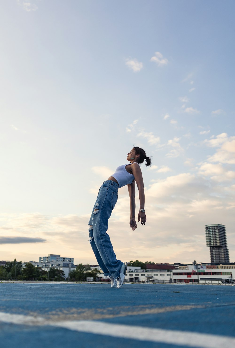 Hombre con camiseta blanca sin mangas y jeans vaqueros azules saltando en el aire durante el día