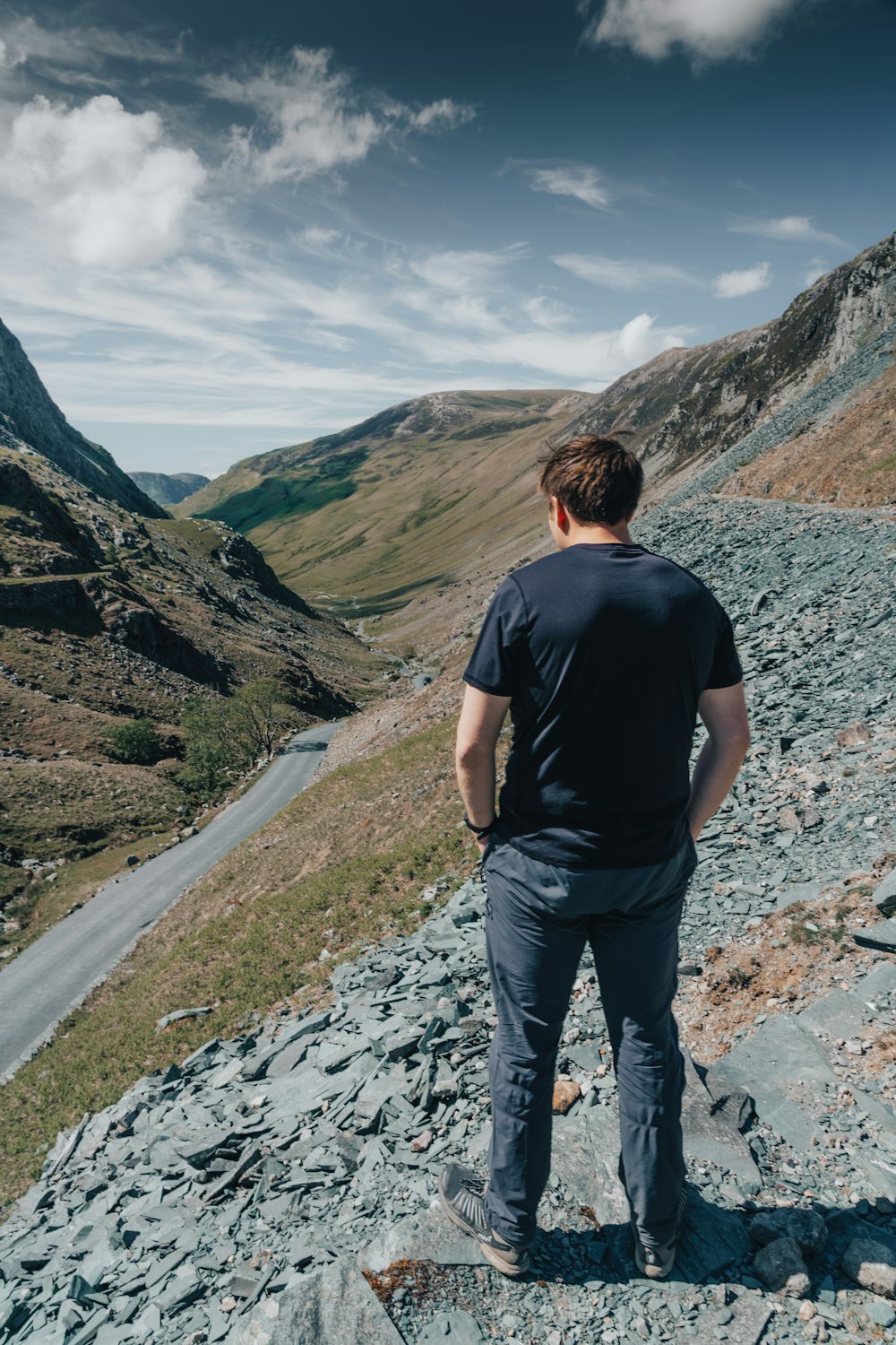man in black t-shirt and black pants standing on rocky road during daytime