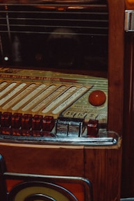 A vintage jukebox with intricate details, featuring a selection panel with various buttons and song slots. The surface is wooden with metallic and glass elements, giving it a classic, retro appearance.
