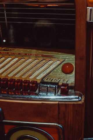 A vintage jukebox with intricate details, featuring a selection panel with various buttons and song slots. The surface is wooden with metallic and glass elements, giving it a classic, retro appearance.