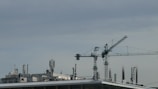 Crane lifting heavy electrical transformers onto a warehouse rooftop.