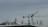 Cranes towering over a building rooftop with various antennas and equipment, set against a cloudy sky.