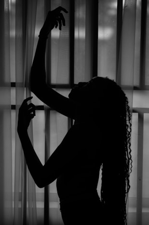 A silhouette of a model framed by sheer curtains, highlighting graceful curves.