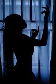 Close-up of hands in a graceful Pilates pose with olive and blue light filtering through sheer curtains.