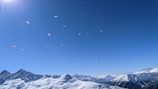 Colorful paragliders soaring above the mountainous terrain of Issarbe Altitude on a clear day.