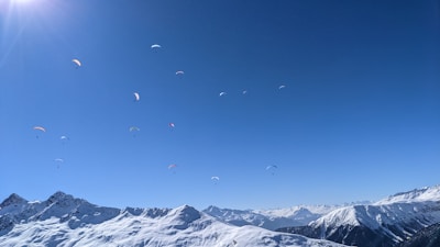 Colorful paragliders soaring above the mountainous terrain of Issarbe Altitude on a clear day.