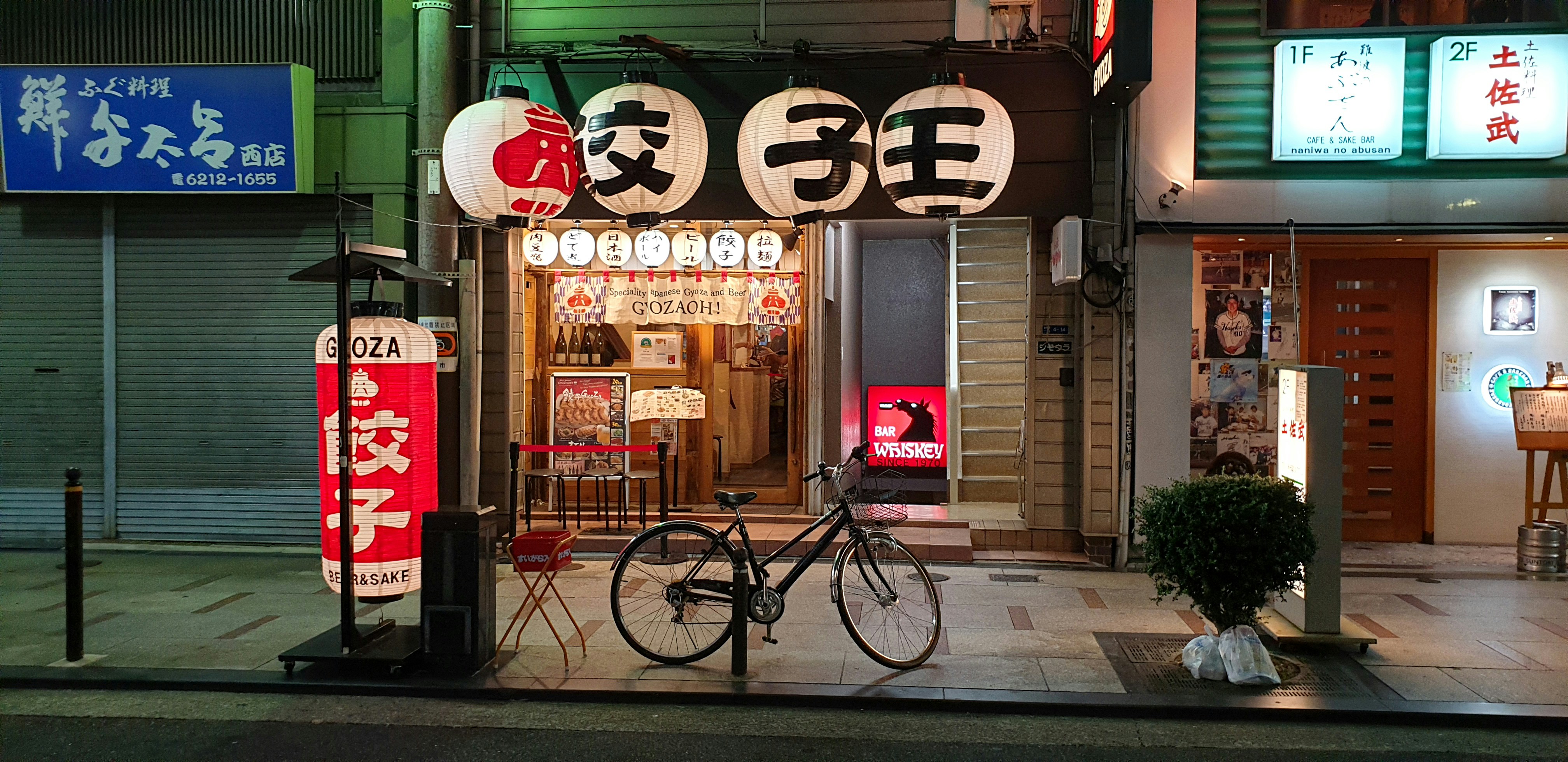 red and black bicycle parked beside store during daytime, Gyoza restaurant with large lanterns and bicycle in Osaka.